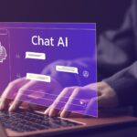the image of a person working on a laptop with focus on their hands. The inscription “Chat AI” can be read on the screen and a stylized chat program can be seen.