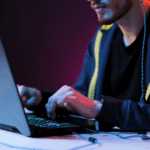 A young man is typing on a laptop in a dark room.